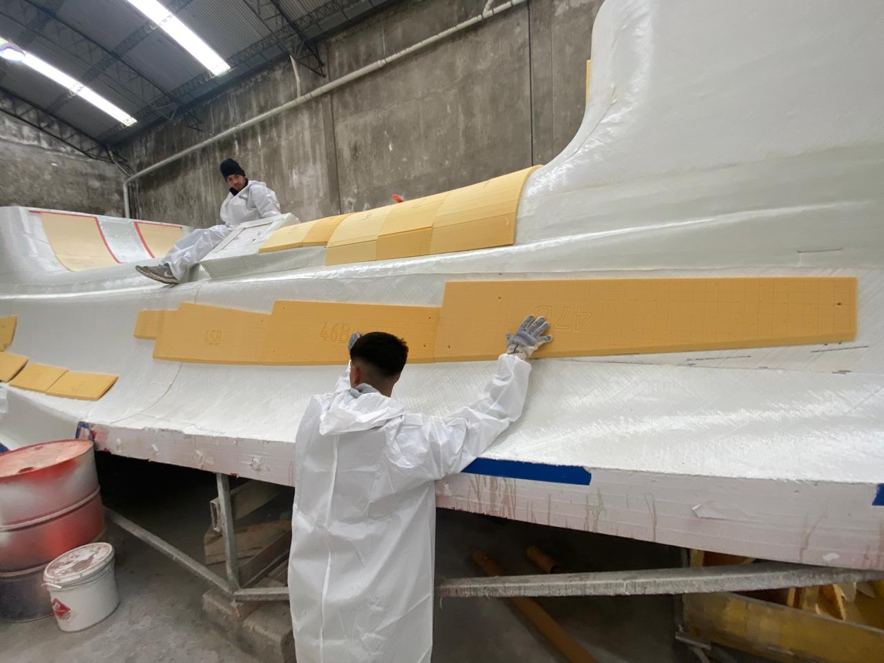 Technicians hand-laying foam core panels onto a fiberglass hull mold